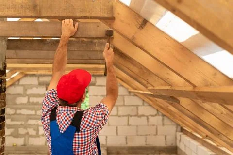 Construction worker in uniform and red cap installing wooden beams and plan.. Stock Photos