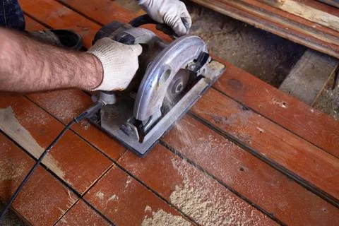A construction worker uses a circular saw to cut wooden planks in a workshop Stock Photos