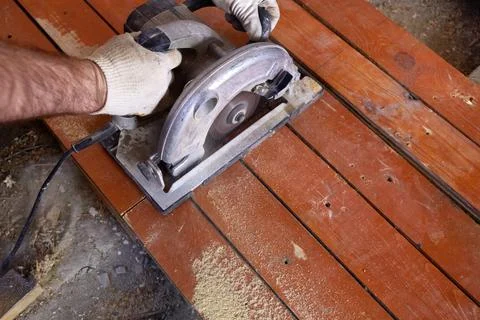 A construction worker uses a circular saw to cut wooden planks in a workshop Stock Photos