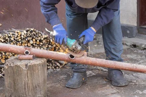 A construction worker uses an electric angle grinder to cut a metal pipe ou.. Stock Photos