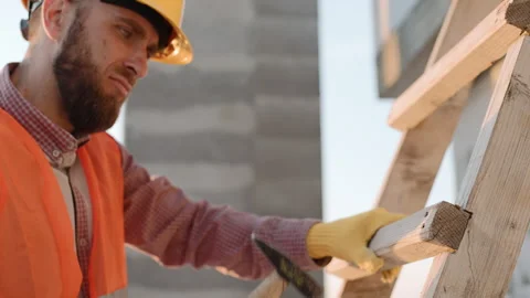 Construction worker uses hammer to secure wooden beams on site in clear weather Vídeos de archivo 295959419