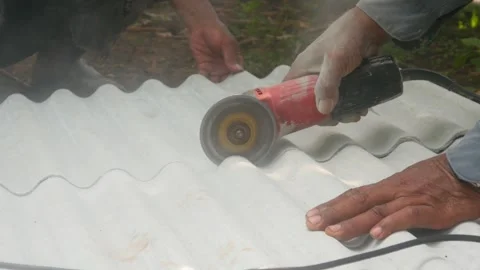 A construction worker uses a hand grinder to cut asbestos Stock Footage 333346779