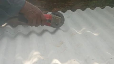 A construction worker uses a hand grinder to cut asbestos Stock Footage 333346783