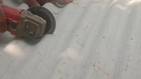 A construction worker uses a hand grinder to cut asbestos Stock Footage 333346844