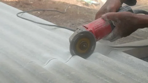 A construction worker uses a hand grinder to cut asbestos Stock Footage 333346871
