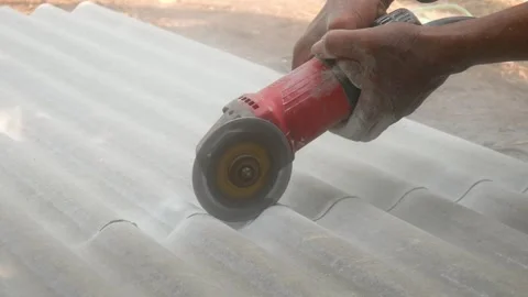 A construction worker uses a hand grinder to cut asbestos Stock Footage 333346878