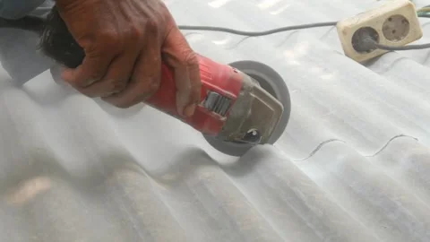 A construction worker uses a hand grinder to cut asbestos Stock Footage 333346893