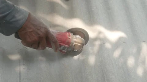 A construction worker uses a hand grinder to cut asbestos Stock Footage 333346913