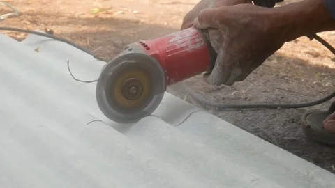 A construction worker uses a hand grinder to cut asbestos Stock Footage 333346914