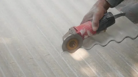 A construction worker uses a hand grinder to cut asbestos Stock Footage 333346924