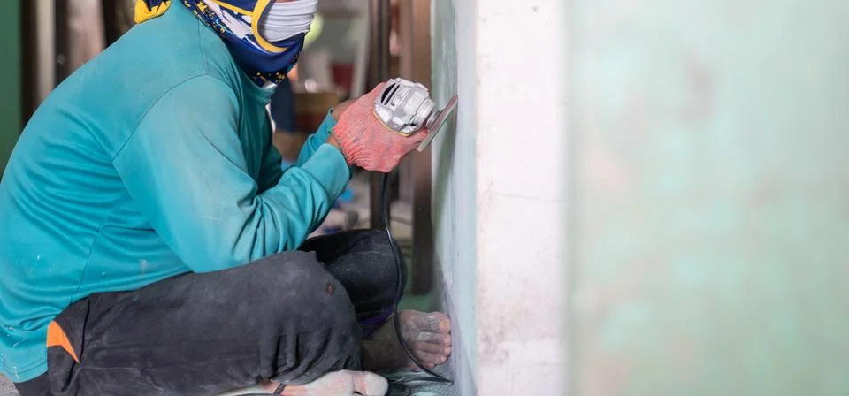 Construction worker uses a handheld power sander to remove old paint dust f.. Stock Photos