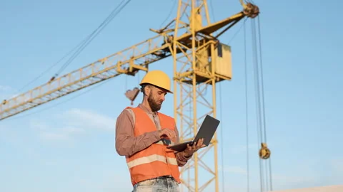 Construction worker uses laptop on site while crane operates in background Video stock 311308427