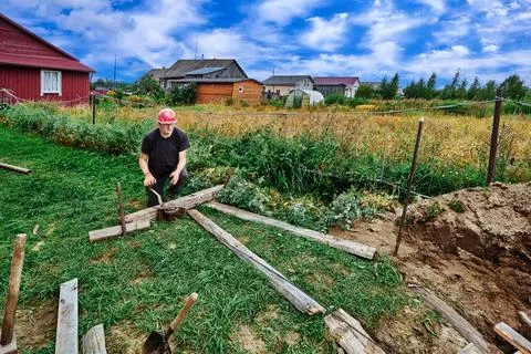 Construction worker uses manual cable winch to move load on suburban property Fotos de archivo