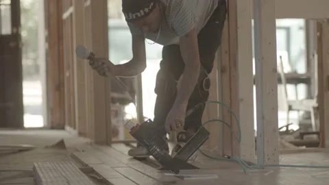 Construction worker uses a nail gun to install flooring Stock Footage