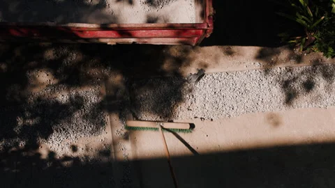 Construction worker uses a push broom to sweep crushed stone into an excavated Stock Footage 341470076