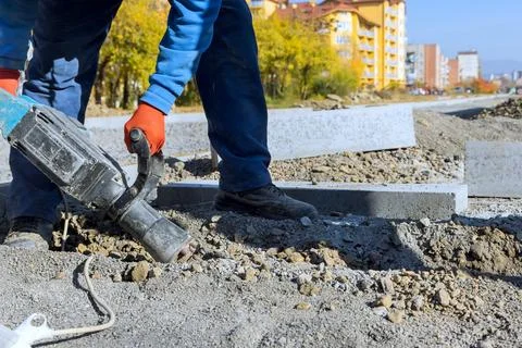Construction worker uses tool to break ground on road project in an urban are Stock Photos