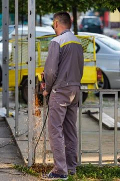 Construction Worker Using Angle Grinder on Metal Post Producing Sparks at O.. Stock Photos