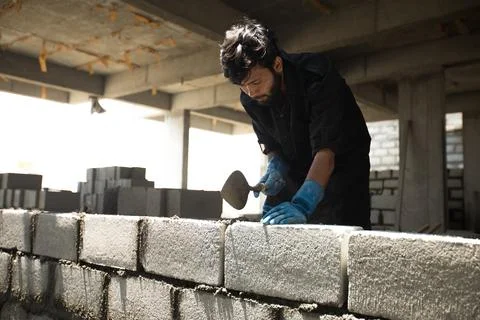 A construction worker using bricks and cement between them. Stock Photos