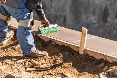 Construction Worker Using Brush On Wet Cement Forming Coping Around New Pool. Foto stock