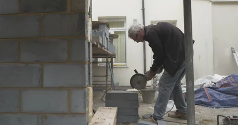 Construction worker using circular saw to cut through breeze block Stock Footage 246380655