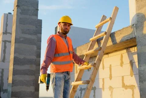 Construction worker using cordless drill on wooden ladder at building site Stock Photos