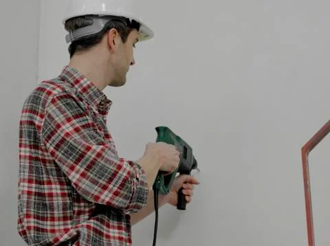 A construction worker using a drill on a wall Stock Photos
