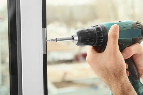 Construction worker using drill while installing window indoors, closeup Stock Photos
