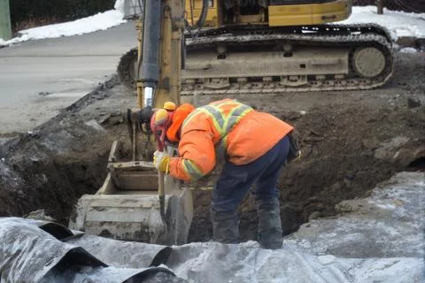 A construction worker using an excavator and a hand shovel to repair a road.. Foto stock