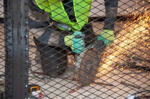 Construction worker using a grinder with sparks flying behind a metal fence Stock Photos