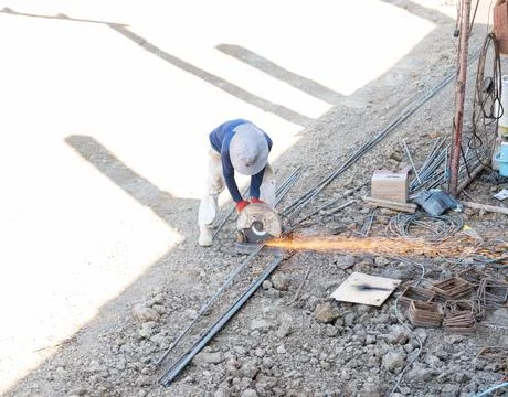 A construction worker using a metal chop saw to cut steel rebar. Stock Photos