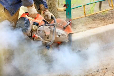 A construction worker using a portable gasoline saw cuts a concrete curb for  Stock Photos