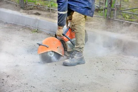 A construction worker using a portable gasoline saw cuts old asphalt to repai Stock Photos