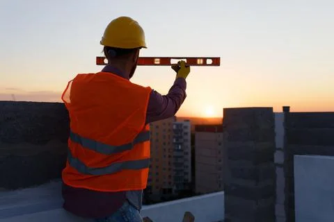 Construction worker using spirit level at building site with crane in backg.. Stock Photos