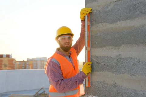 Construction worker using spirit level on building site at sunset Stock-Fotos