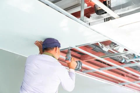 A construction worker, viewed from the back, is installing a white gypsum p.. Stock-Fotos