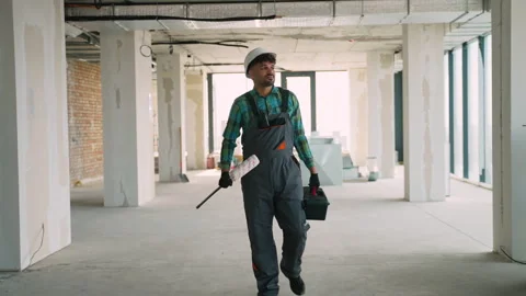 Construction worker walking in unfinished building carrying paint roller and Stock Footage 312840040