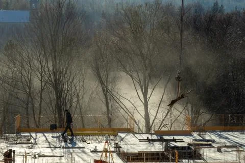 A construction worker walks across an active site at sunrise, where a crane Stock Photos