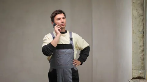 Construction worker wearing overalls using smartphone in unfinished building Stock Footage 314082956