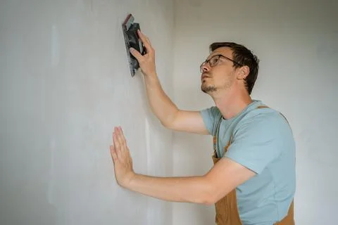 Construction worker wearing protective eyewear and work attire sanding freshly Stock Photos