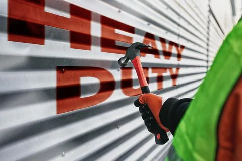 Construction worker wearing protective gloves holds a hammer against a meta.. Stock Photos