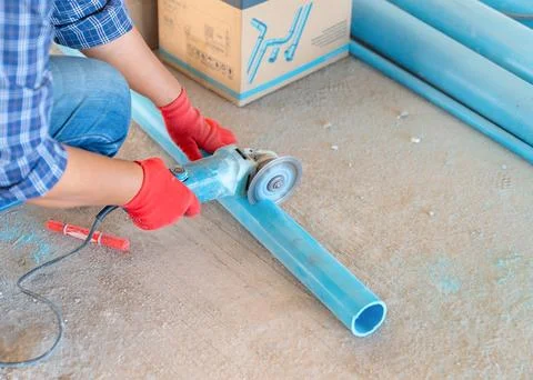 A construction worker wearing red protective gloves cuts a blue PVC pipe wi.. Stock Photos