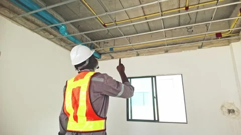 Construction worker wearing safety gear inspects exposed ceiling wiring. 動画素材 311374872