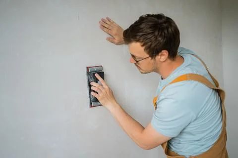 Construction worker wearing safety glasses and denim overalls sanding concrete Stock Photos