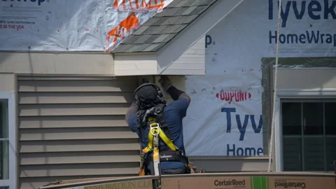 Construction worker wearing safety harness installs exterior wall siding on 库存影片 327917850