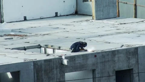 Construction worker welding metal on rooftop of concrete building under Stock Footage 344864274