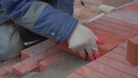 A construction worker in white gloves lays the sidewalk with an orange brick Stock Footage 291198933