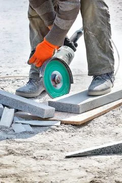 A construction worker in work clothes and orange gloves leans over and cuts t Stock Photos