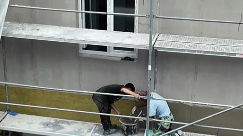 Construction workers apply plaster to insulated wall on scaffolding Stock Footage 338333035