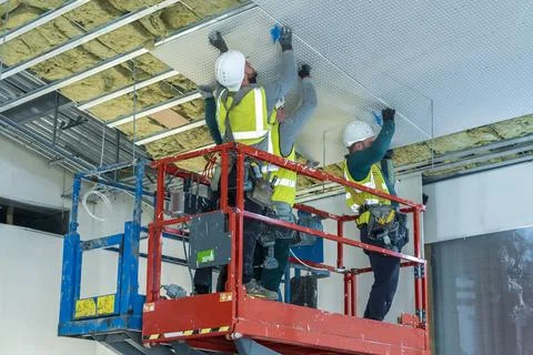 Construction workers are diligently installing ceiling panels in a modern Stock Photos