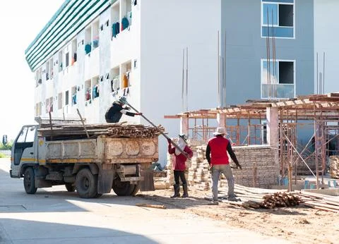 Construction workers are unloading wooden poles from a truck at a building .. Stock Photos